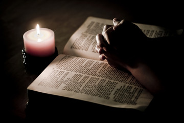 Praying hands on top of bible, lit by candle light © munchkinmoo