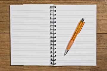Open spiral notebook with pen on wooden table.