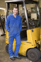 Warehouse worker standing by forklift