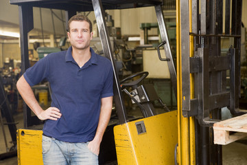 Warehouse worker standing by forklift