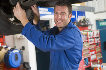 Mechanic working under car smiling
