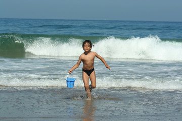 petit garçon entrain de courir avec un seau sur la plage