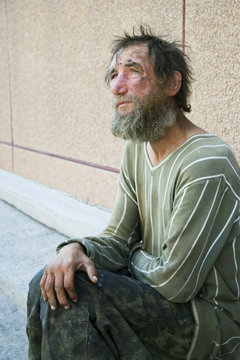 Sad homeless man sitting on at the wall on city street