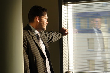 sad business man looking through window blinds