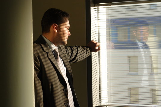 Sad Business Man Looking Through Window Blinds