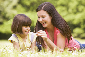 Mother and daughter lying outdoors with flower smiling