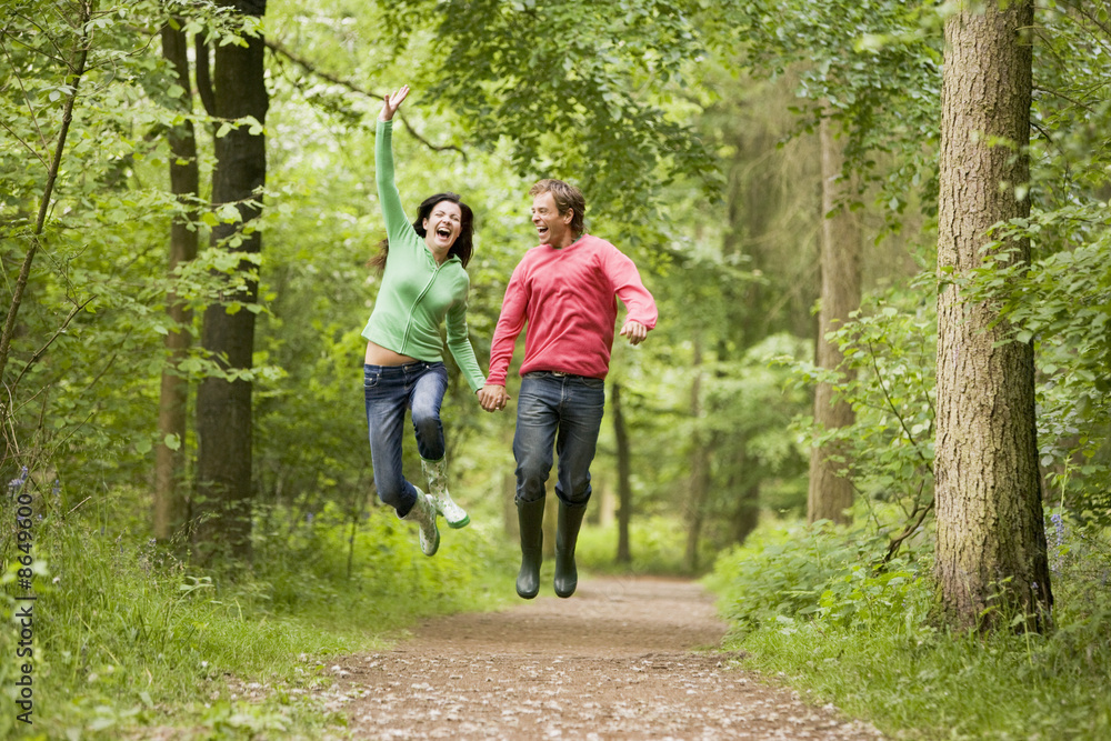 Wall mural couple jumping on path holding hands and smiling