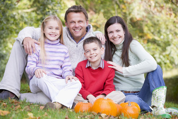 Fototapeta premium Family sitting on grass with pumpkins smiling