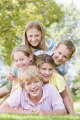 Five young friends piled on each other outdoors smiling