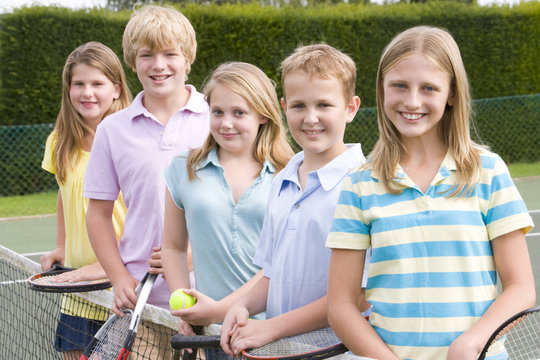 Five young friends with rackets on tennis court smiling
