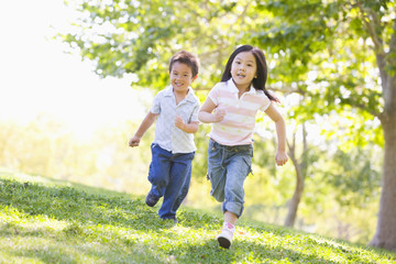 Brother and sister running outdoors smiling