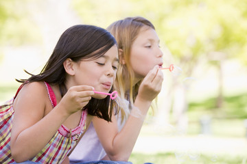 Two young girls blowing bubbles outdoors