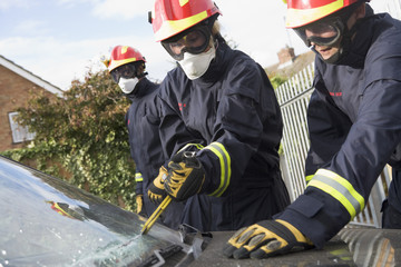 Firefighters breaking a car windscreen to help car crash victim