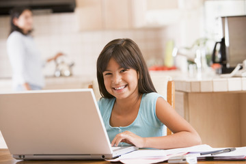 Young girl in kitchen with laptop and paperwork smiling with wom