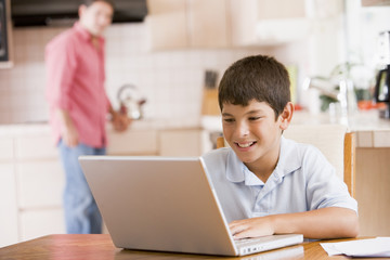 Young boy in kitchen with laptop and paperwork smiling with man