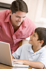 Obraz premium Man helping young boy in kitchen with laptop smiling