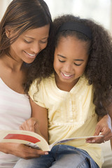 Obraz premium Woman and young girl sitting in living room reading book and smi