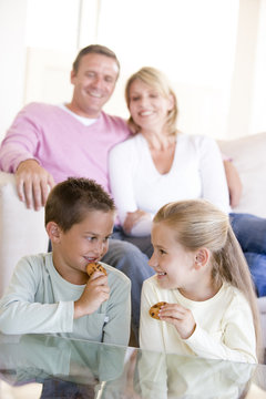 Family Sitting In Living Room Eating Cookies And Smiling