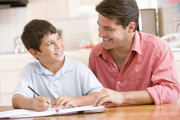 Obraz premium Man helping young boy in kitchen doing homework and smiling