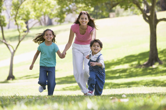 Woman with two young children running outdoors smiling