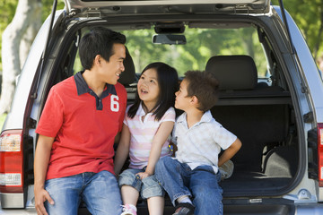 Man with two children sitting in back of van smiling