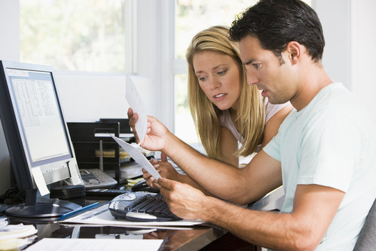 Couple in home office with computer and paperwork looking unhapp