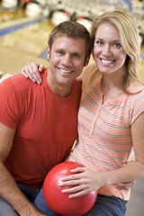 Couple in bowling alley holding ball and smiling