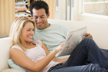 Couple in living room reading newspaper and smiling
