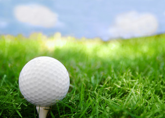 Golf ball closeup, on the tee, with grass and sky