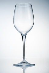 Empty wine glass on reflective surface over light background
