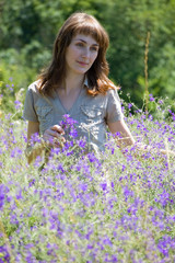The girl walks across the field and collects wild flowers