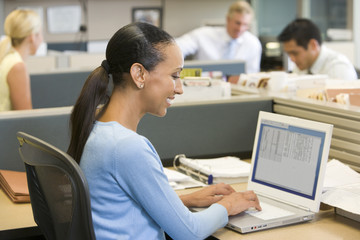 Businesswoman in cubicle using laptop smiling