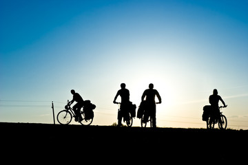 Obraz na płótnie Canvas Group of Bicycle tourists on a road against sunset