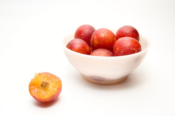 Plums at bowl and  one plum on white background