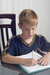 Naklejka premium Boy doing homework sitting at a dining table
