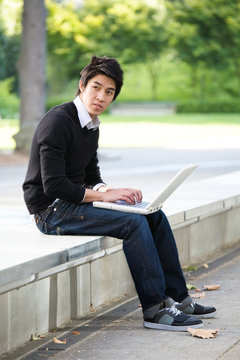 An asian student working on his laptop at the campus