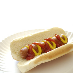 Hot dog on a bun on a white plate with ketchup and mustard