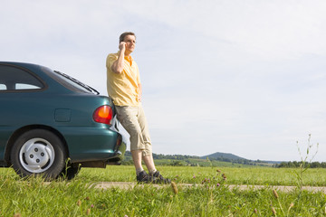 Mann telefoniert mit Handy neben seinem Auto