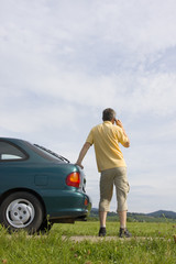 Mann telefoniert mit Handy neben seinem Auto