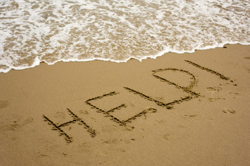 The word "HELP" written on a sandy beach with water