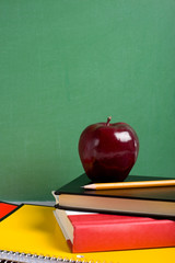 school books and an apple in front of a  blank chalkboard