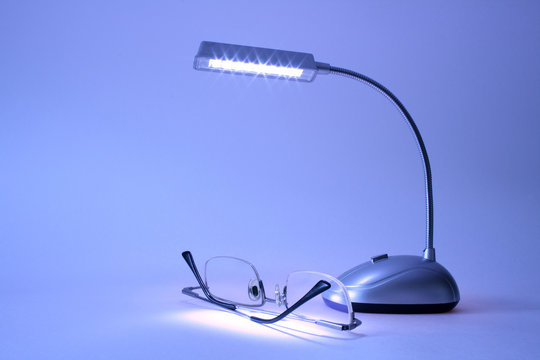 Table lamp and modern spectacles lying on blue background