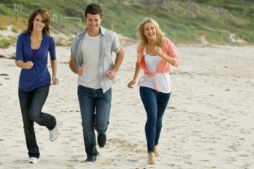Three friends running along a sandy beach in autumn