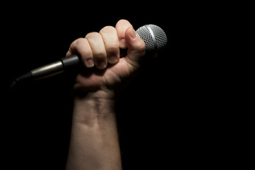 Microphone clinched firmly in male fist on a black background.