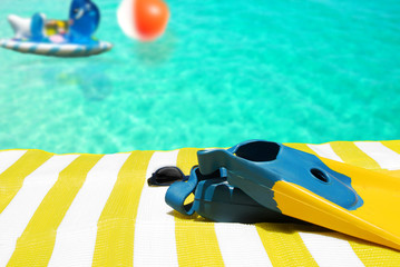 Swimming fins and toys by beach towel and pool