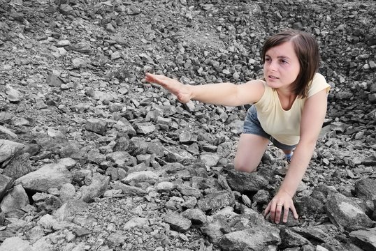 Young woman needs help and stretches her hand from rocky hole