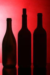 Silhouettes of three wine bottles against red background