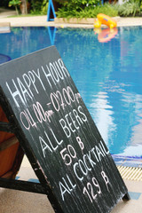Happy hour sign next to a swimming pool.