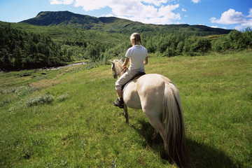 Fototapeta na wymiar Rear view of young woman riding horse in rural setting