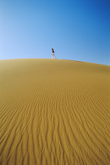Fototapeta na wymiar Woman walking across desert sand dune